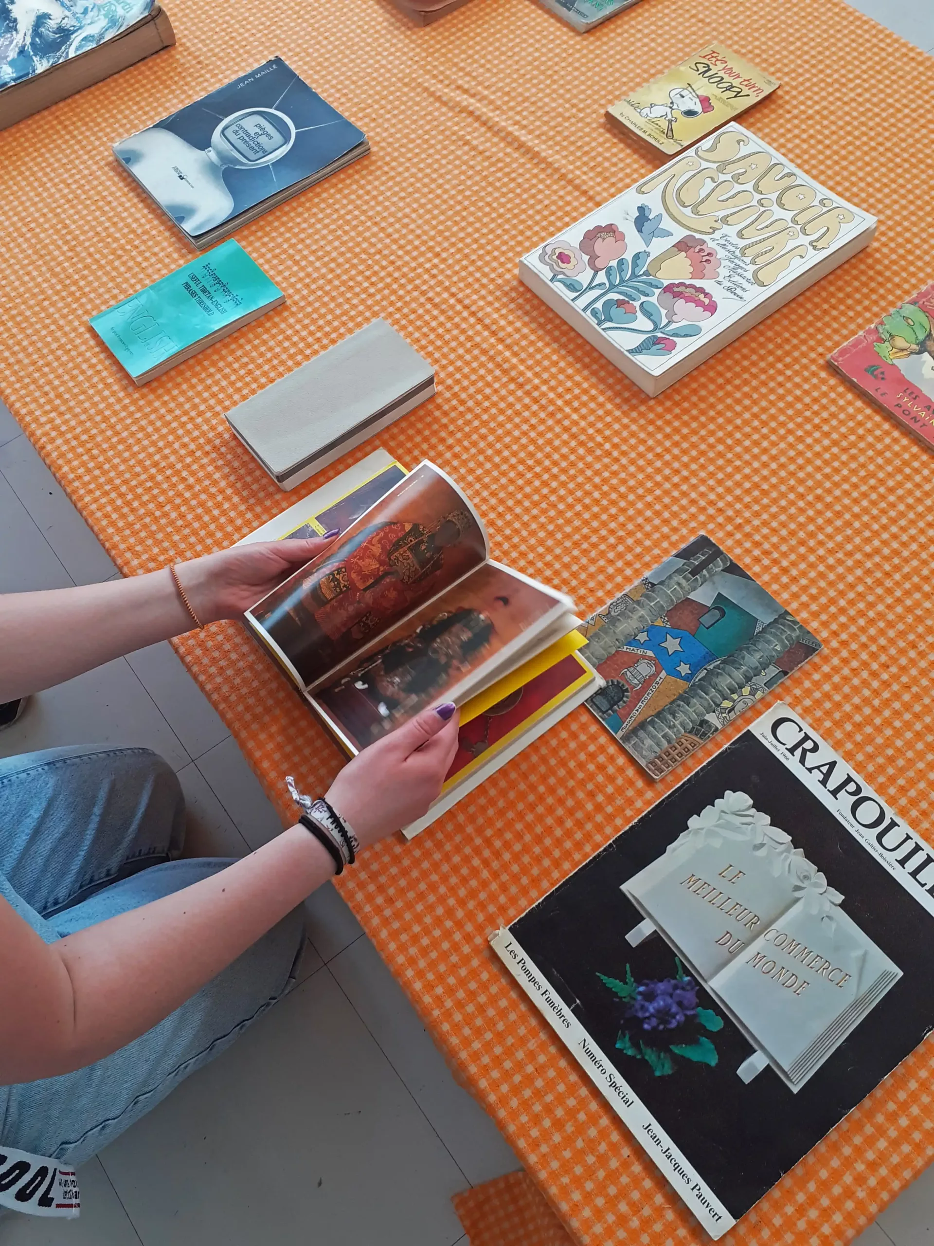Photo d'une personne qui feuillette un livre sur une table basse, entourée d'autres livres.